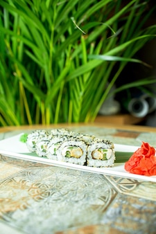 Vue latérale de sushi set rouleaux avec du fromage à la crème de chair de crabe et de l'avocat dans du caviar de poisson volant servi avec des tranches de gingembre sur vert