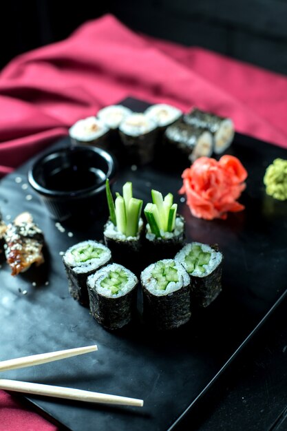 Vue latérale de sushis noirs végétariens roule avec des concombres servis avec du gingembre et de la sauce soja sur tableau noir