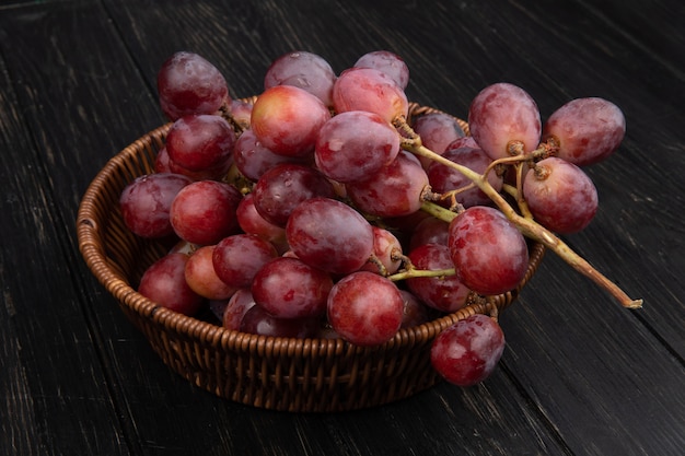 Vue latérale d'un tas de raisins doux frais dans un panier en osier sur une table en bois foncé