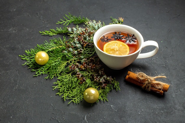 Vue latérale d'une tasse d'accessoires de thé noir et de limes à la cannelle sur fond noir