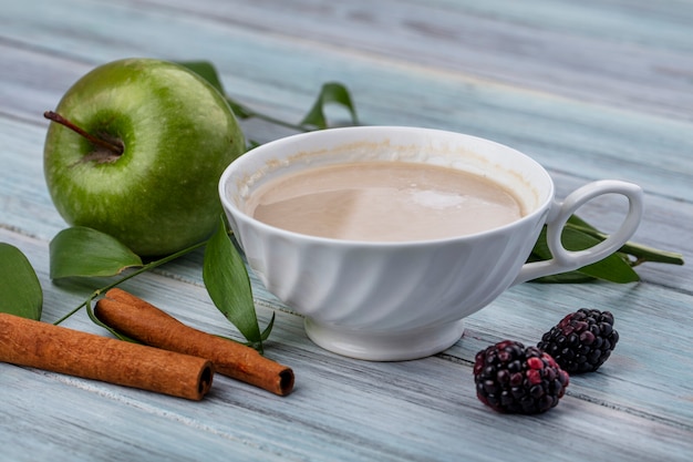 Vue latérale d'une tasse de cappuccino avec de la cannelle et de la pomme verte sur une surface grise