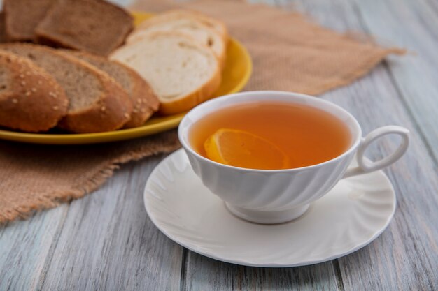 Vue latérale d'une tasse de hot toddy sur soucoupe avec des pains tranchés dans une assiette sur un sac sur fond de bois