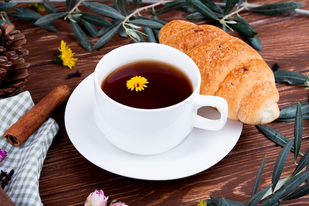 Vue latérale d'une tasse de thé avec croissant et pissenlits sur bois