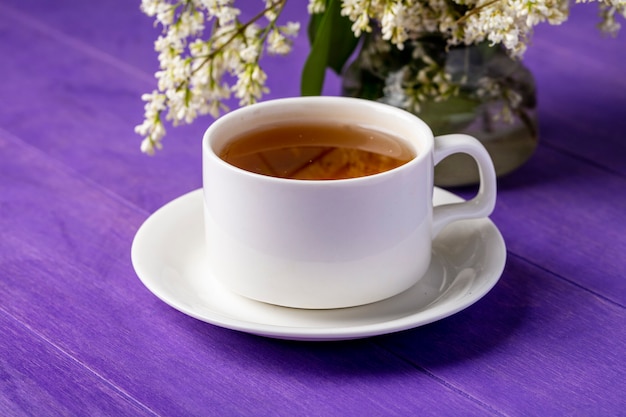 Vue latérale d'une tasse de thé avec des fleurs sur une surface violet vif