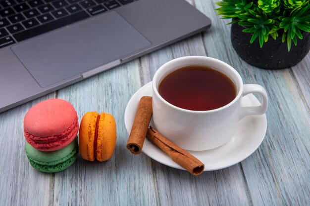 Vue latérale d'une tasse de thé avec des macarons de couleur cannelle et un ordinateur portable sur une surface grise