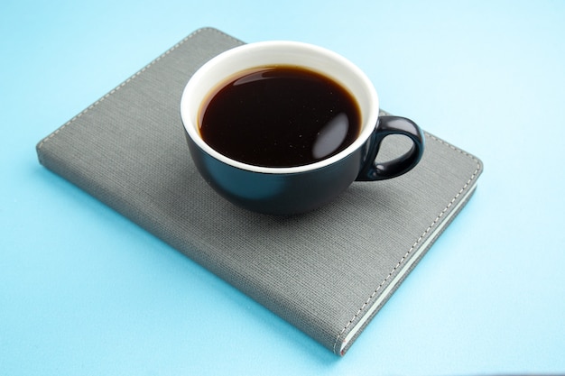 Vue latérale d'une tasse de thé noir sur un cahier gris sur une surface bleue