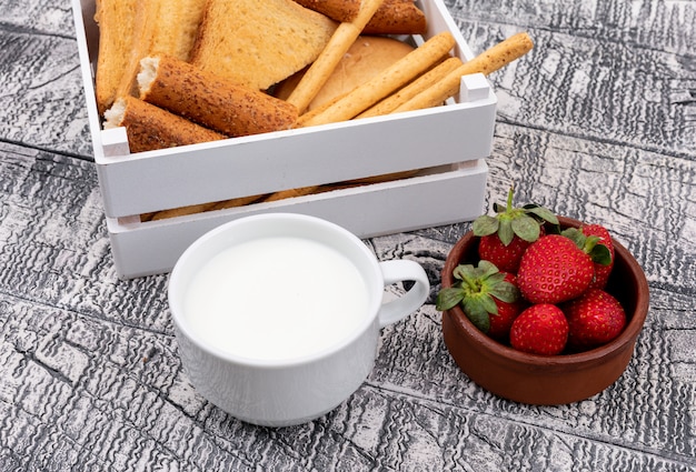 Vue latérale des toasts avec du lait dans la caisse et la fraise sur la surface blanche horizontale