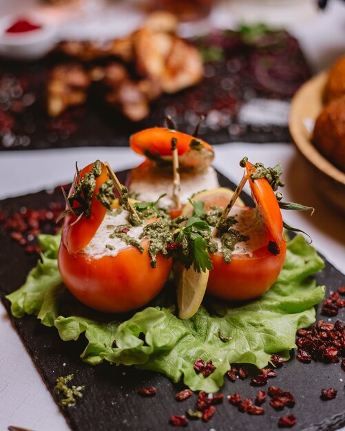 Vue latérale des tomates farcies avec sauce à la crème sauce pesto verte et épine-vinette séchée sur une plaque