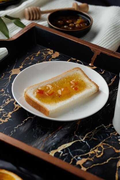 Vue latérale d'une tranche de pain enduite de confiture dans le bac et de confiture avec une louche de miel sur un tissu sur fond noir