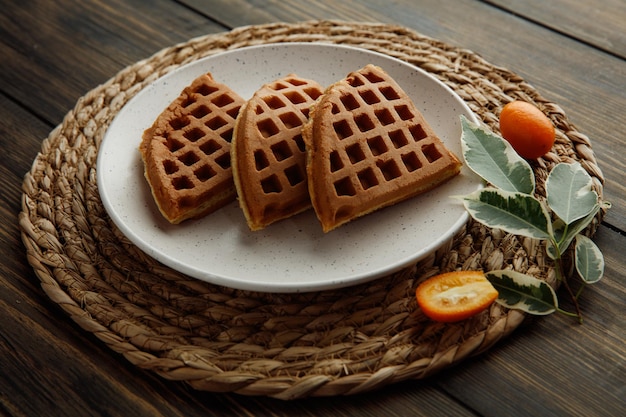 Vue latérale des tranches de crêpes dans une assiette sur un trépied avec des kumquats coupés et entiers et des feuilles sur un trépied sur fond de bois