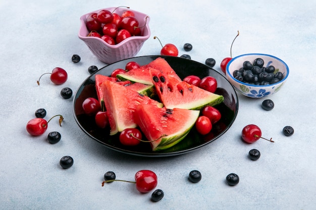 Vue latérale des tranches de pastèque sur une assiette avec des myrtilles et des cerises