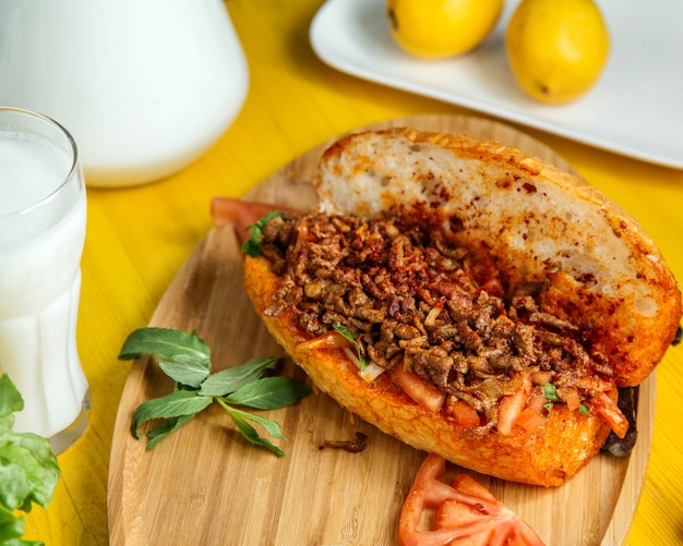 Vue latérale de la viande hachée avec des légumes dans du pain servi avec des tomates fraîches et du citron sur une planche de bois