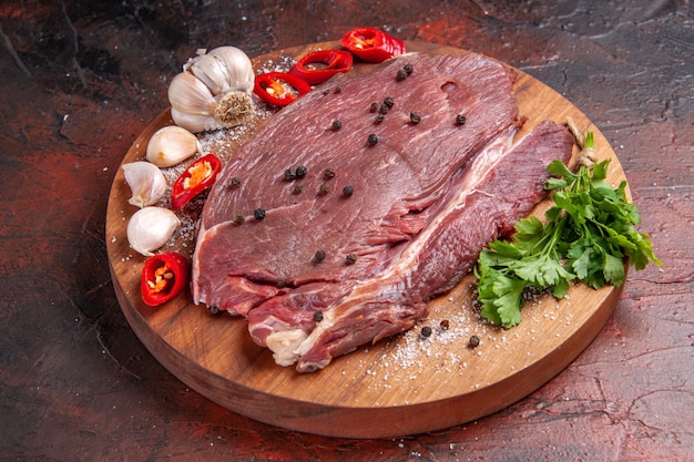 Vue latérale de la viande rouge sur un plateau en bois et de l'oignon citron vert à l'ail sur fond sombre