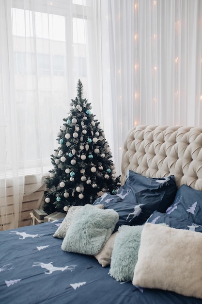 Vue sur lit fait avec beau drap avec cerf et coussins. Le mur décoré de guirlande. La chambre décorée pour Noël avec sapin.