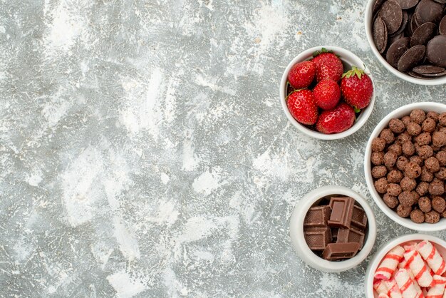 Vue lointaine du haut des bols avec des bonbons fraises chocolats amers et laiteux céréales et cacao sur le côté droit du sol gris-blanc