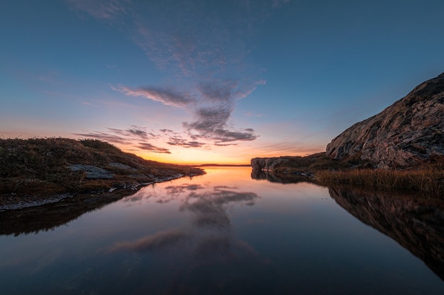 Vue magnifique sur un lac calme entouré de rochers, avec le ciel reflété sur l'eau pendant le coucher du soleil