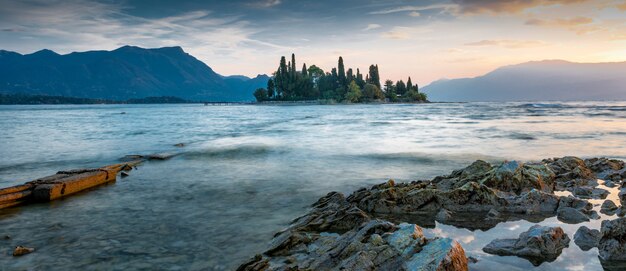 Vue d'une mer avec une petite île pleine d'arbres au milieu avec les montagnes