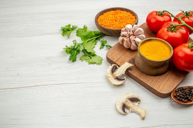 Vue de la moitié inférieure du bol de curcuma à l'ail de branche de tomate fraîche sur un bol de lentilles de champignons de planche à découper sur un espace libre de table gris