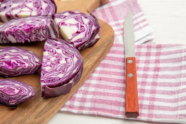 Vue de la moitié inférieure du chou rouge haché sur un couteau de planche à découper sur un torchon à carreaux rose et blanc sur une table grise