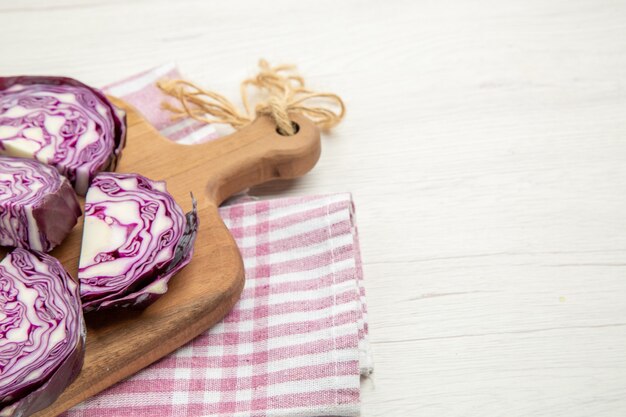 Vue de la moitié inférieure du chou rouge haché sur une planche à découper sur un torchon à carreaux rose et blanc sur une table grise avec un espace libre