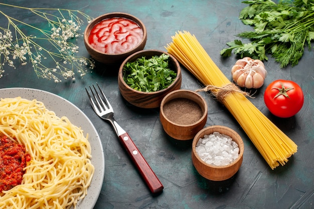 Photo gratuite vue de la moitié des pâtes italiennes cuites avec de la viande et différents assaisonnements sur une surface bleue