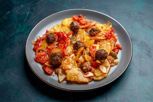 Vue de la moitié des pommes de terre au four avec boulettes de viande et légumes à l'intérieur de la plaque sur fond bleu foncé.