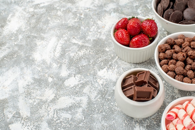 Vue de la moitié supérieure des bols avec des bonbons blanc-rouge fraises chocolats céréales et cacao sur le côté droit du sol gris-blanc