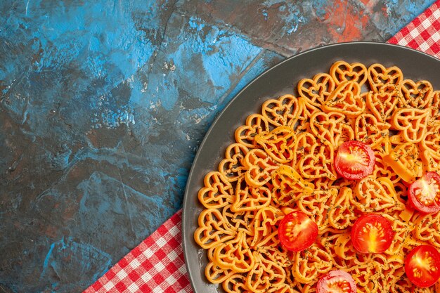 Vue de la moitié supérieure des coeurs de pâtes italiennes coupées de tomates cerises sur une plaque ovale sur une nappe à carreaux rouges et blancs