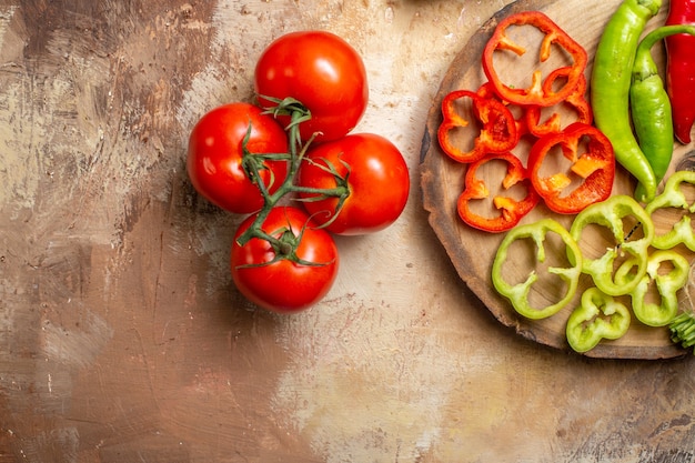 Vue de la moitié supérieure de différents légumes piments forts poivrons coupés en morceaux sur une planche de bois d'arbre rond tomates sur fond ocre jaune