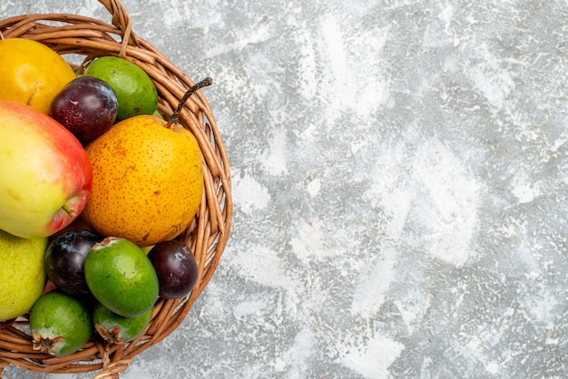 Photo gratuite vue de la moitié supérieure du panier en osier en plastique avec des poires aux pommes, des prunes feykhoas et du kaki sur la table grise