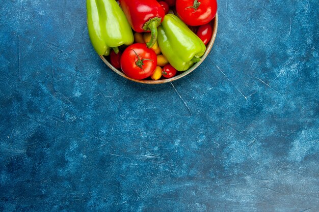 Vue de la moitié supérieure des légumes tomates cerises poivrons de différentes couleurs tomates dans un bol sur table bleue avec copie place