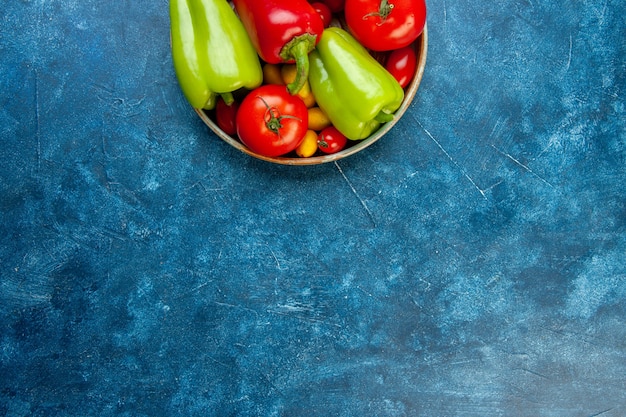 Vue de la moitié supérieure des légumes tomates cerises poivrons de différentes couleurs tomates dans un bol sur table bleue avec copie place