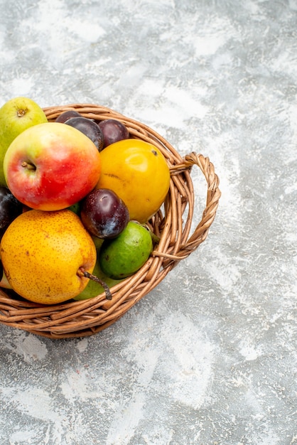 Photo gratuite vue de la moitié supérieure panier en osier en plastique avec des poires aux pommes, des prunes feykhoas et du kaki à gauche de la table grise