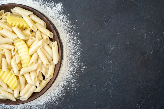 Vue de la moitié supérieure des pâtes penne savoureuses avec des pommes de terre dans un bol saupoudré de farine sur la table