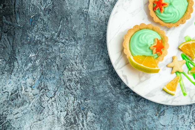 Vue de la moitié supérieure de petites tartelettes avec de la crème pâtissière verte et une tranche de citron sur une plaque sur une surface sombre de l'espace libre