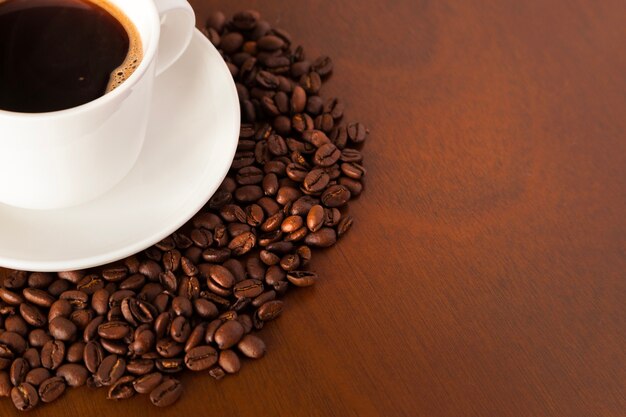 Vue partielle de la tasse de café et des haricots sur la table en bois