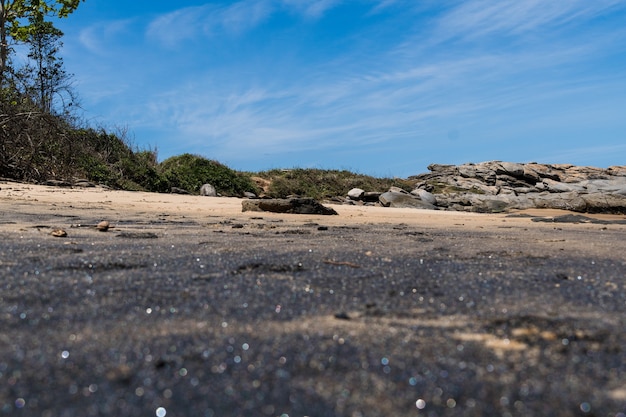 Vue sur la plage d'areia negras à rio das ostras à rio de janeiro avec journée ensoleillée, ciel bleu et quelques nuages. mer forte et sable noir mêlé de jaune et de nombreux rochers.