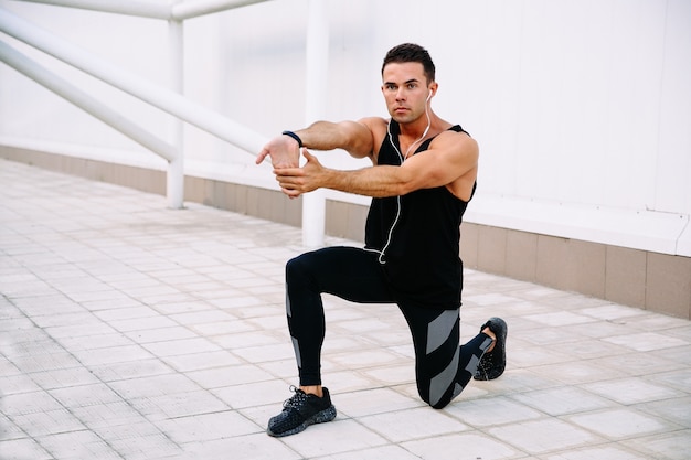 Vue de pleine longueur de gars sportif faisant des exercices physiques pour les bras et les jambes, s&#39;étendant à l&#39;extérieur