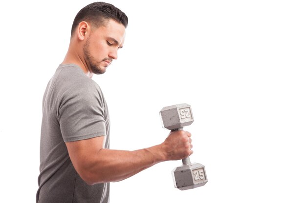 Vue de profil d'un gars fort soulevant des poids et renforçant ses bras sur un fond blanc