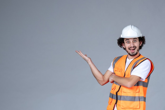 Vue rapprochée d'un architecte masculin curieux en gilet d'avertissement avec casque de sécurité sur un mur gris vague