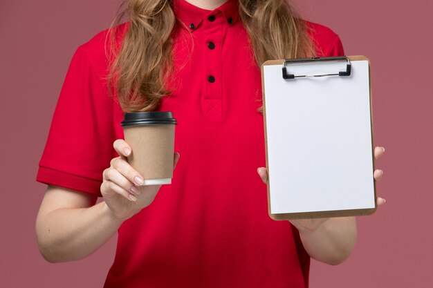 Vue rapprochée avant de courrier féminin en uniforme rouge tenant le bloc-notes et la tasse de café sur rose, prestation de services de travailleur uniforme de travail