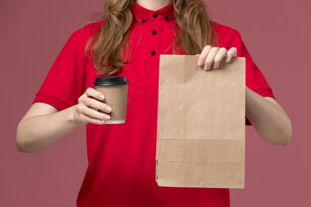 Vue rapprochée avant de courrier féminin en uniforme rouge tenant un paquet de nourriture et une tasse de café sur rose, travailleur de travail de livraison de service uniforme