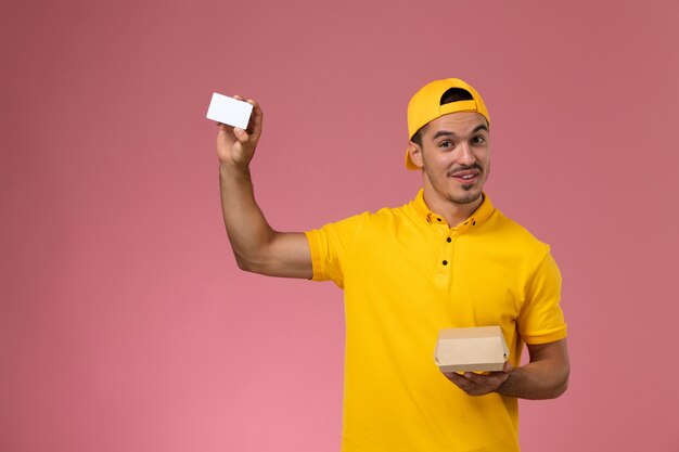 Vue rapprochée avant de courrier masculin en uniforme jaune tenant la carte et petit paquet de nourriture sur le mur rose