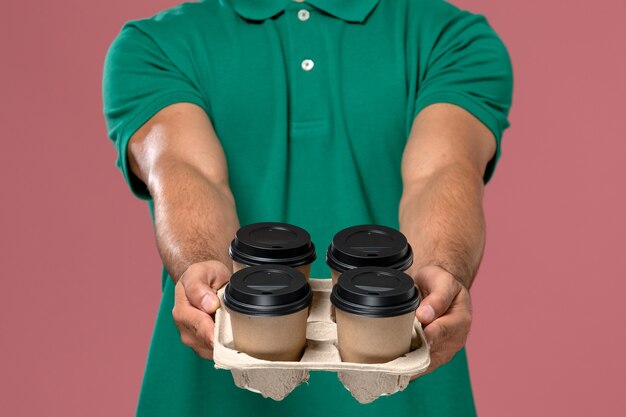 Vue rapprochée avant de courrier masculin en uniforme vert tenant des tasses à café sur le rose