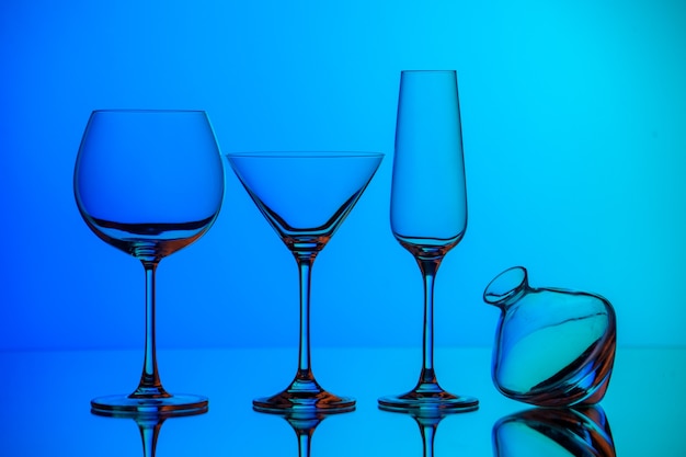 Vue rapprochée avant de divers types de gobelet en verre vide debout sur une surface bleue
