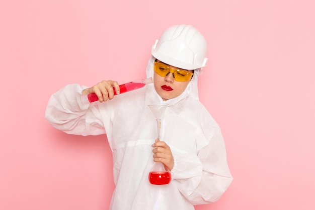 Vue rapprochée avant jeune belle femme en costume blanc spécial portant un casque de protection mélangeant des solutions sur rose