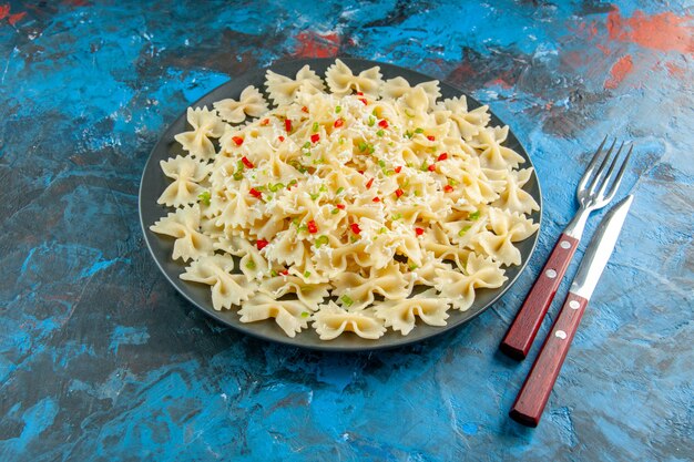 Photo gratuite vue rapprochée avant des pâtes farfalle italiennes crues avec des légumes et des couverts sur fond bleu