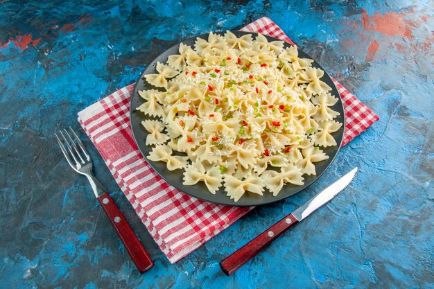 Vue rapprochée avant des pâtes farfalle italiennes crues sur une serviette et des couverts rouges dépouillés sur une table bleue