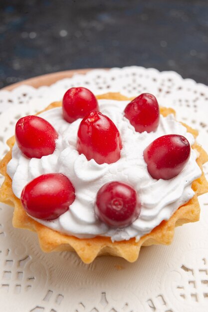 Vue rapprochée avant petit gâteau délicieux avec de la crème et des fruits rouges sur la surface sombre gâteau biscuit aux fruits sucré