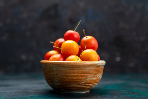 Photo gratuite vue rapprochée avant de prunes cerises fraîches fruits aigres et moelleux à l'intérieur de petit pot sur le fond bleu foncé fruits doux frais vitamine